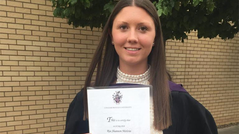 Ria Melvin in her graduation gown, holding her degree certificate.